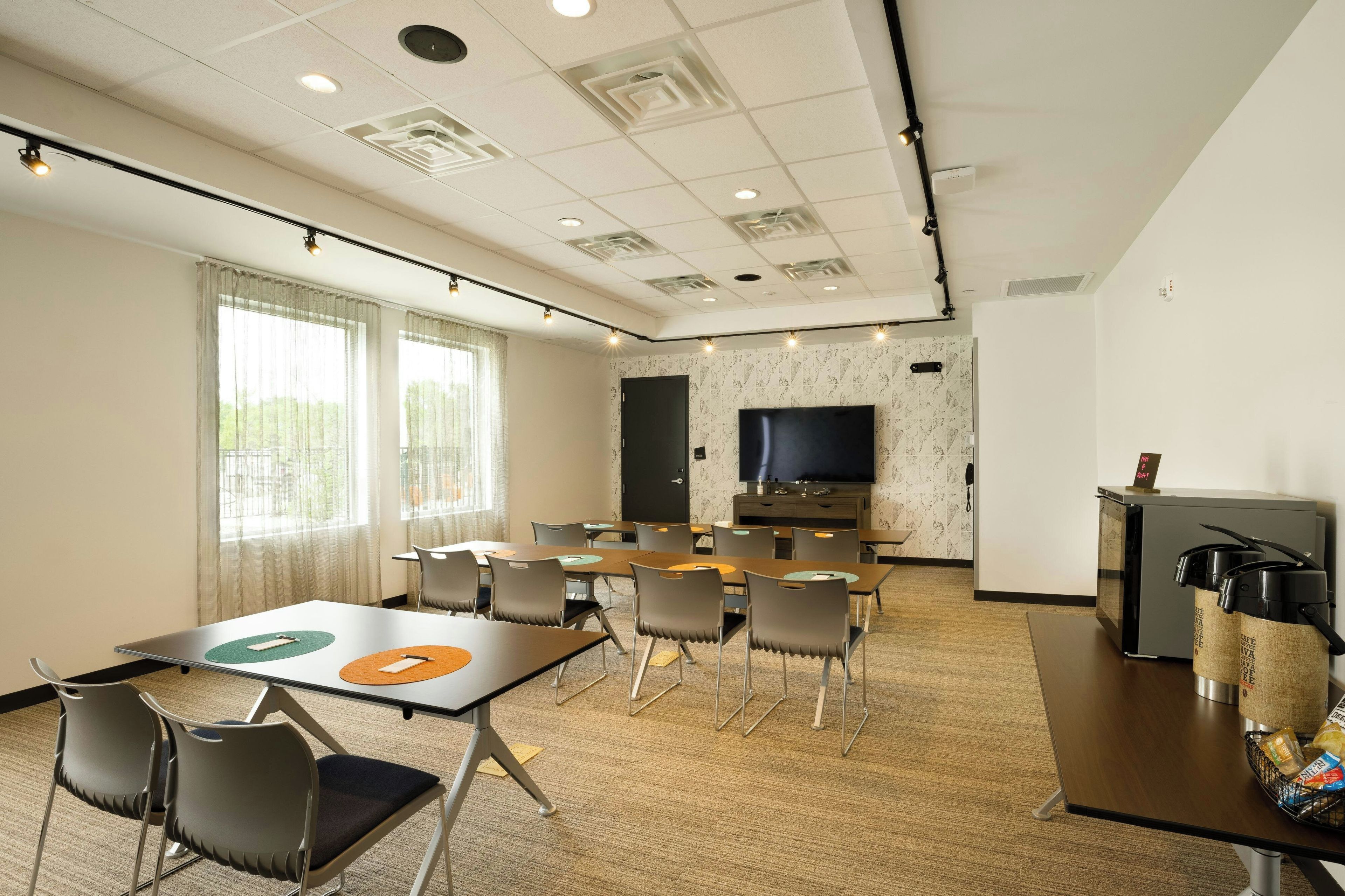 A conference room with a large TV screen, multiple tables, and chairs.