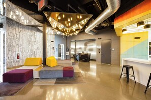 A modern lobby with a reception desk, seating area, and a visible elevator. - Aloft by Marriott Austin Airport (Austin)