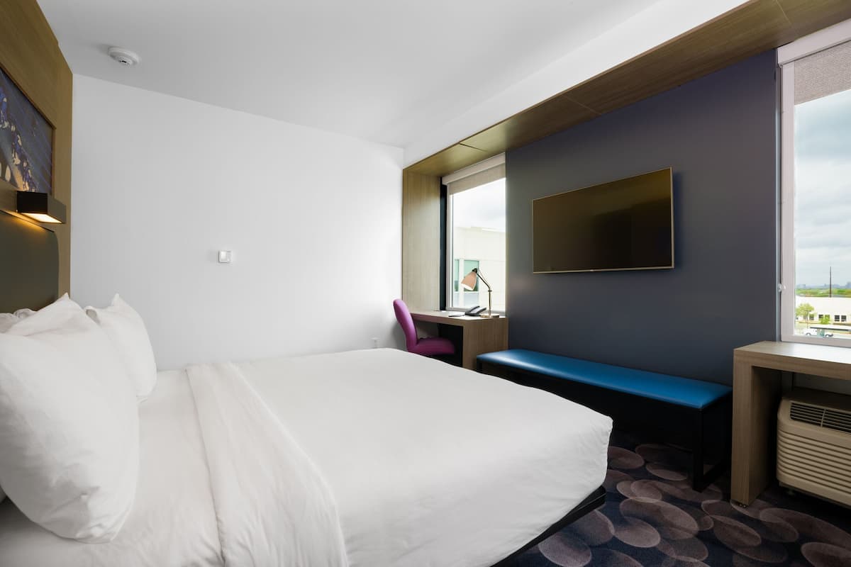 Habitación de hotel con una cama grande, un escritorio con silla, un televisor y una ventana con vistas.