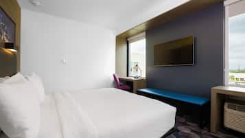 A hotel room with a large bed, a desk with a chair, a TV, and a window with a view.