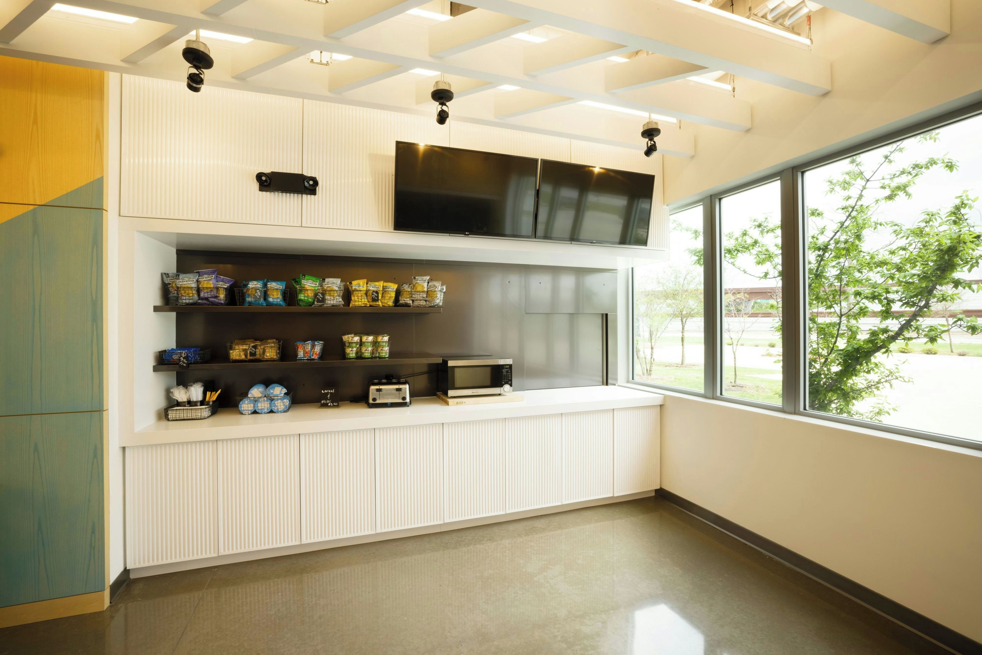 A modern kitchenette with a microwave, toaster, and storage cabinets.