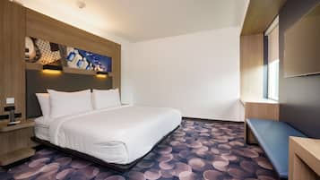 Una habitación de hotel con cama, escritorio, banco y televisor fijado a la pared.