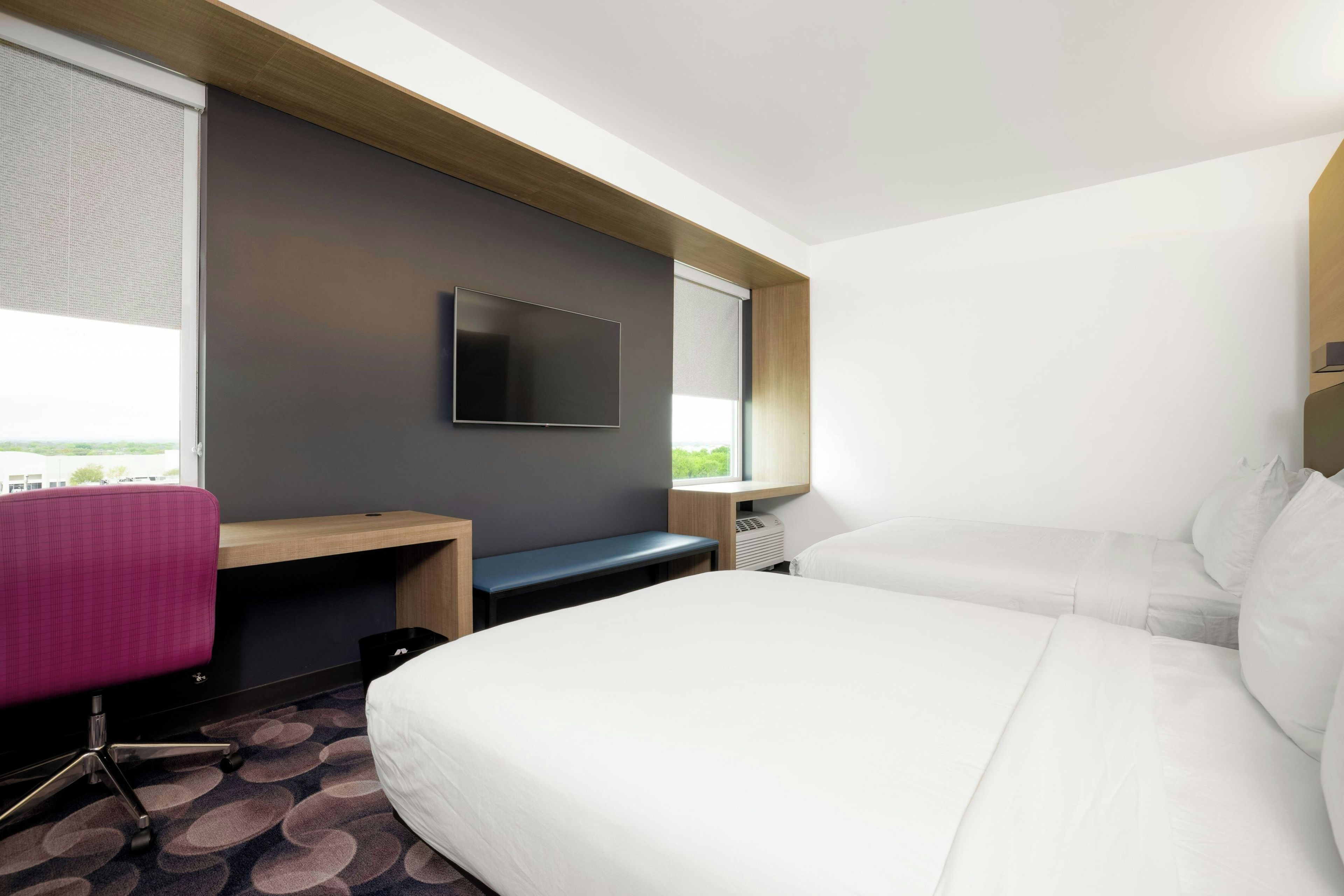 A hotel room with a bed, a desk, a chair, a TV, and a window.