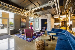 A modern lounge area with a blue sofa, a pink chair, and a colorful rug. - Aloft by Marriott Austin Airport (Austin)