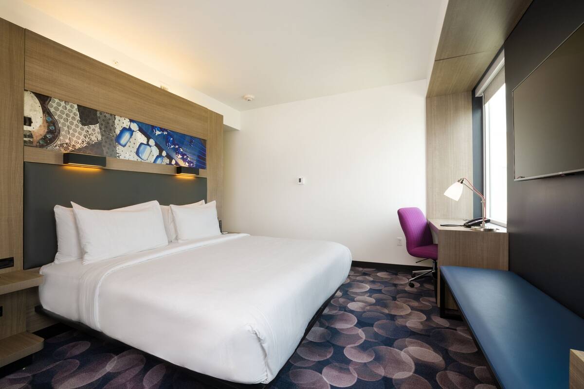 Habitación de hotel con una cama grande, un escritorio, una silla y un televisor montado en la pared.