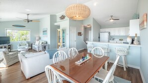 A spacious living room with a dining area, a kitchen, and a balcony. - Blue Haven | Ocean Views, Private Pool + Beach Access! (Surf City)