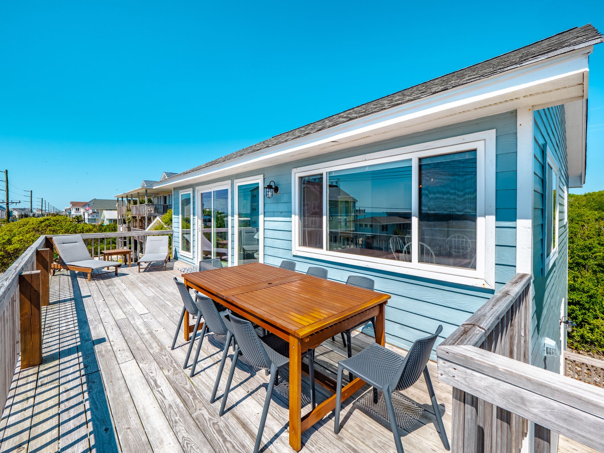 Een houten terras met een tafel en stoelen, een overdekte patio en uitzicht op zee.