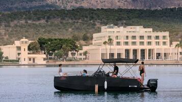 A boat with a black canopy and a Suzuki engine, docked near a building with a white facade and multiple windows.