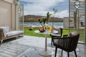 A terrace with a white sofa, a dining table with a bowl of bread and flowers, and a view of a lake and hills.