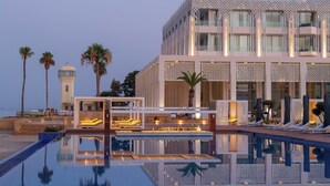 A modern hotel with a pool, lounge chairs, and a view of the sea. - Marchica Lagoon Resort (Beni Ansar)