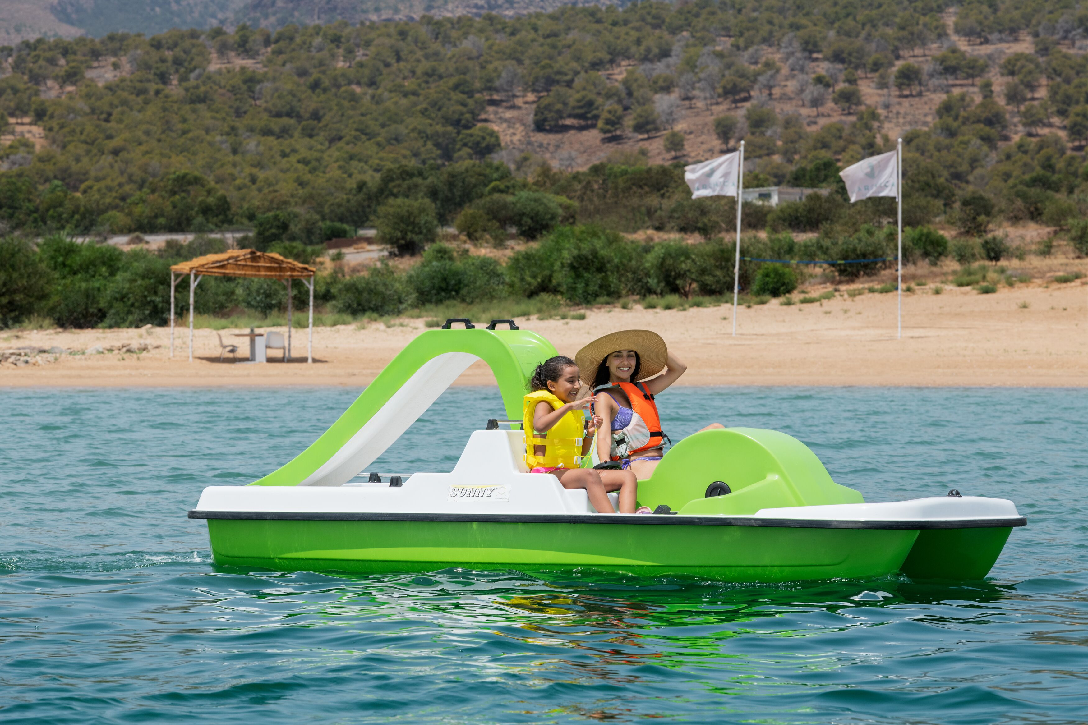 A green boat with two people wearing life jackets on a calm body of water.