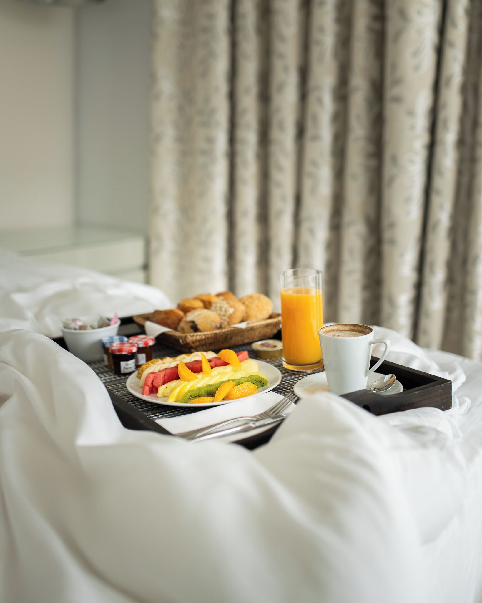 Bandeja de desayuno con frutas, pasteles y un vaso de zumo de naranja sobre una cama.