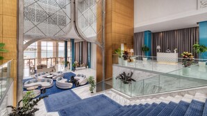 A spacious lobby with a high ceiling, a glass railing, and a seating area with sofas and a coffee table. - Marchica Lagoon Resort (Beni Ansar)