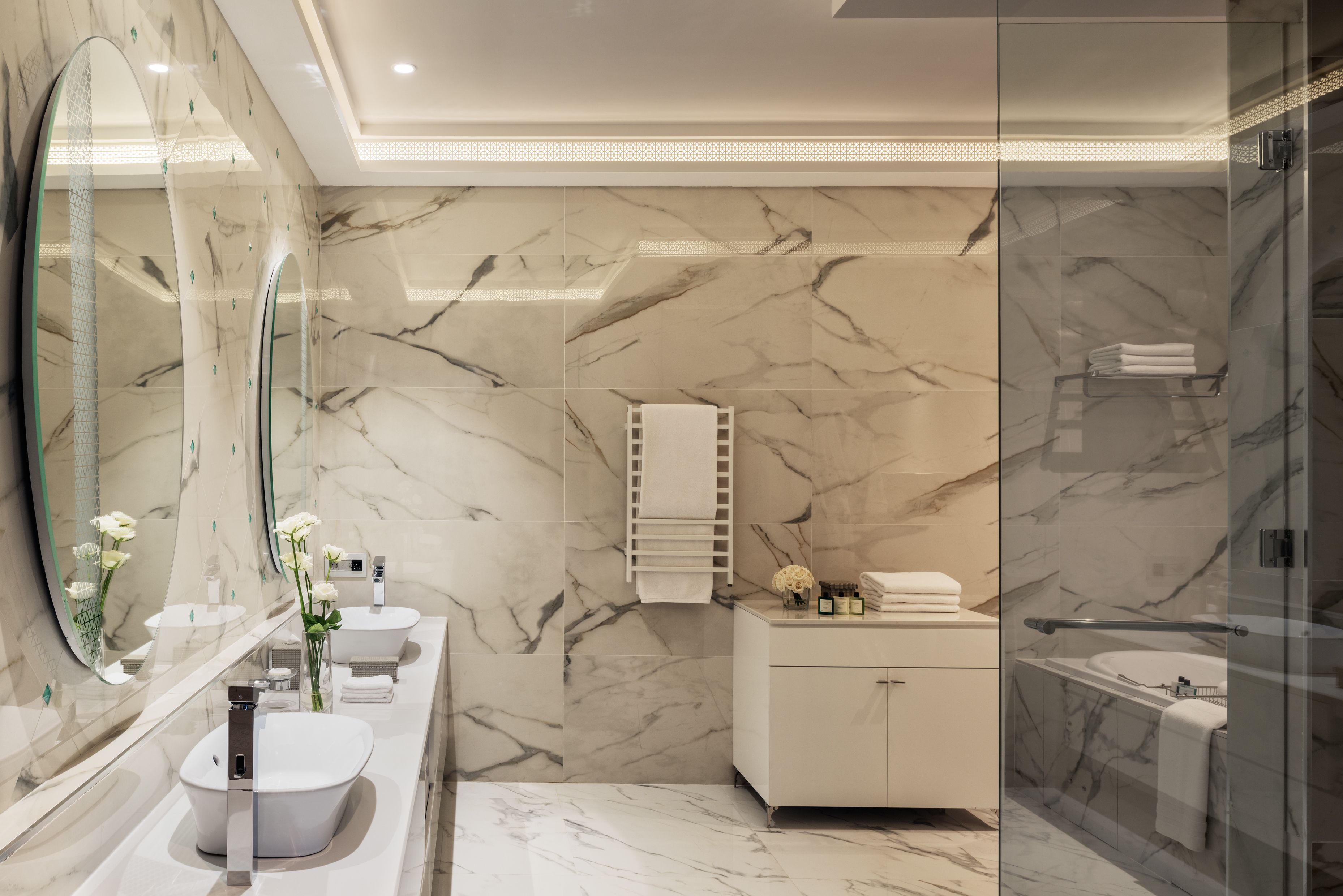 A modern bathroom with marble walls, a glass shower enclosure, and a vanity with two sinks.