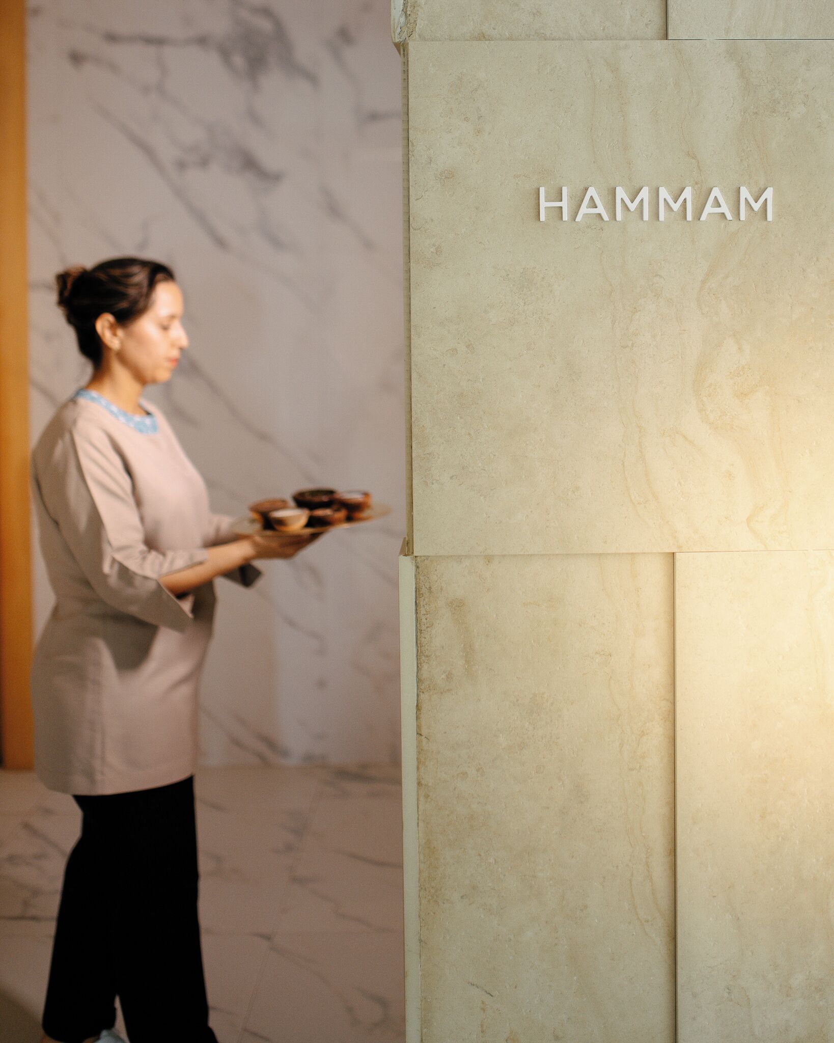 A person holding a book or folder in front of a wall with the word "HAMMAM" on it.
