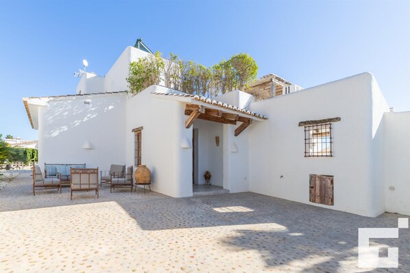 Un edificio blanco con un patio, una pérgola de madera y piso de baldosas.