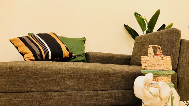 Una sala de estar con un sofá, cojines, una planta pequeña y una cesta decorativa.