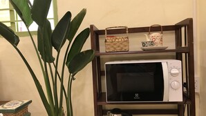 Una cocina con microondas en un estante de madera, una planta en maceta y un hervidor.