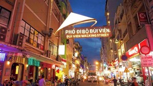 Escena de calle animada con un llamativo letrero iluminado que dice 'PHÒ DI BÒ BUI VIÊN BUI VIÊN WALKING STREET'.