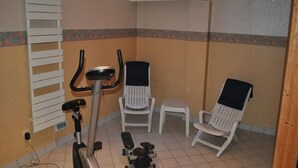 A small, tiled room with a stationary bike, two white chairs, and a small table. - Trip Inn Frankfurt Airport Russelsheim (Ruesselsheim)