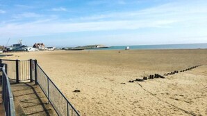 A wide sandy beach with a metal railing and a series of black posts.
