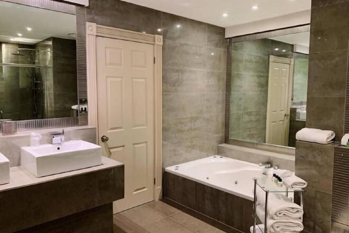 Un baño moderno con un espejo grande, un lavabo blanco, una bañera y un perchero de vidrio.