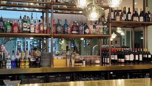 A bar with shelves of liquor bottles and glasses, a bar counter, and hanging light fixtures.