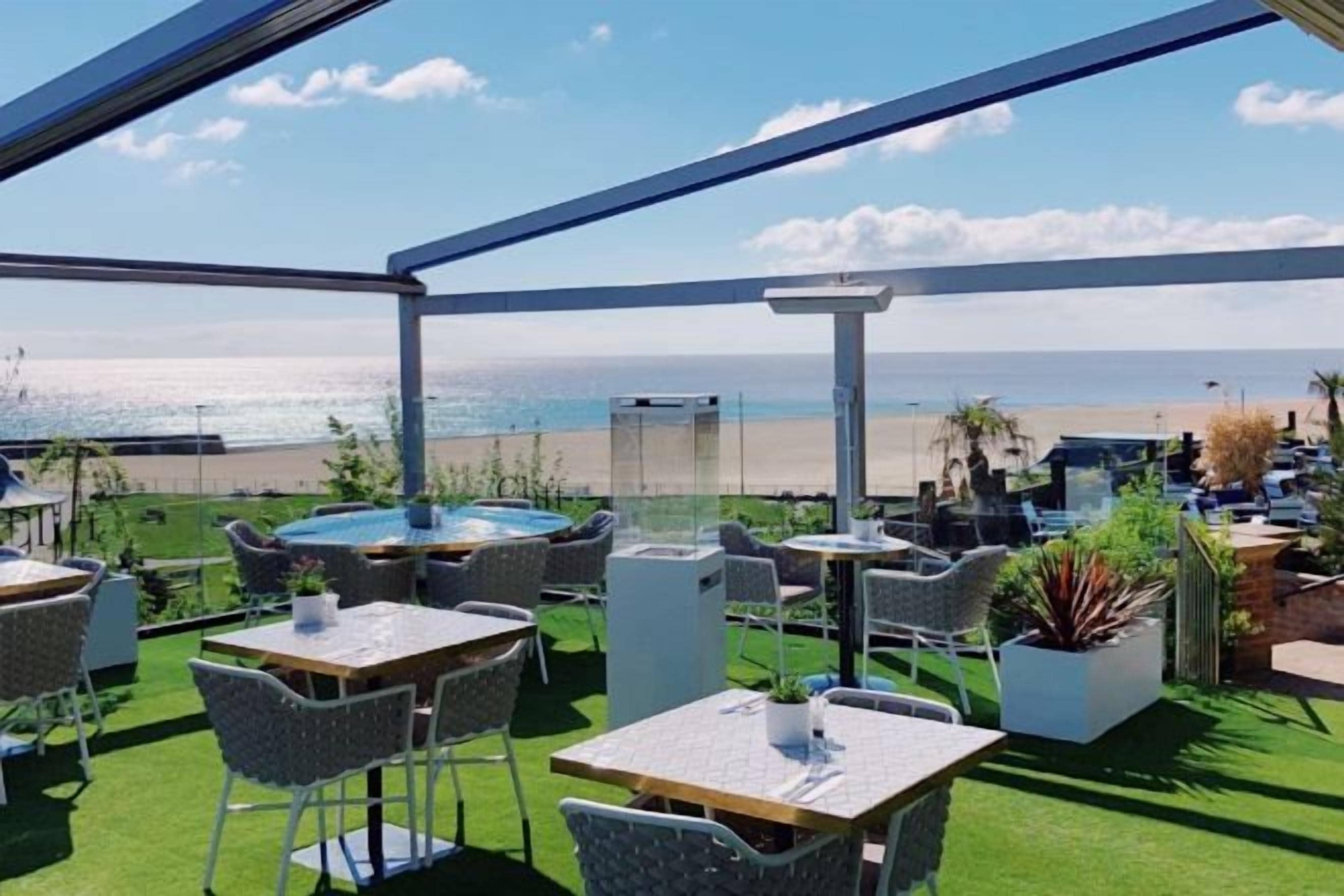 An outdoor seating area with tables and chairs, a hot tub, and a view of the beach.