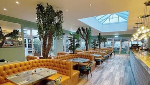 A modern restaurant with leather booths and tables, large windows, and a skylight.