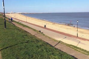 Une promenade en bord de mer, avec une plage, une jetée visible au loin et un ciel dégagé.