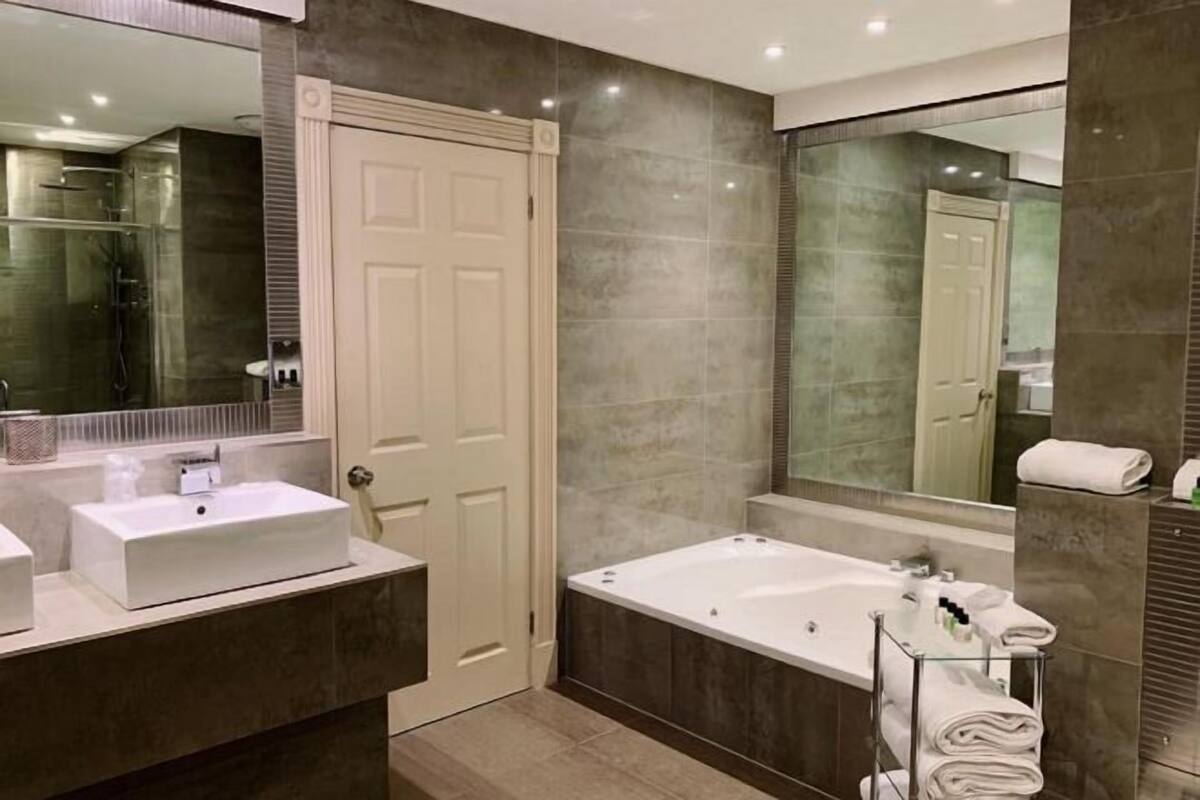 Un baño moderno con un lavamanos blanco, una bañera y un espejo grande.