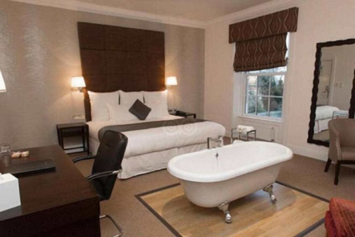 Habitación de hotel con una cama grande, zona de estar con una silla, escritorio, bañera y ventana con vistas.
