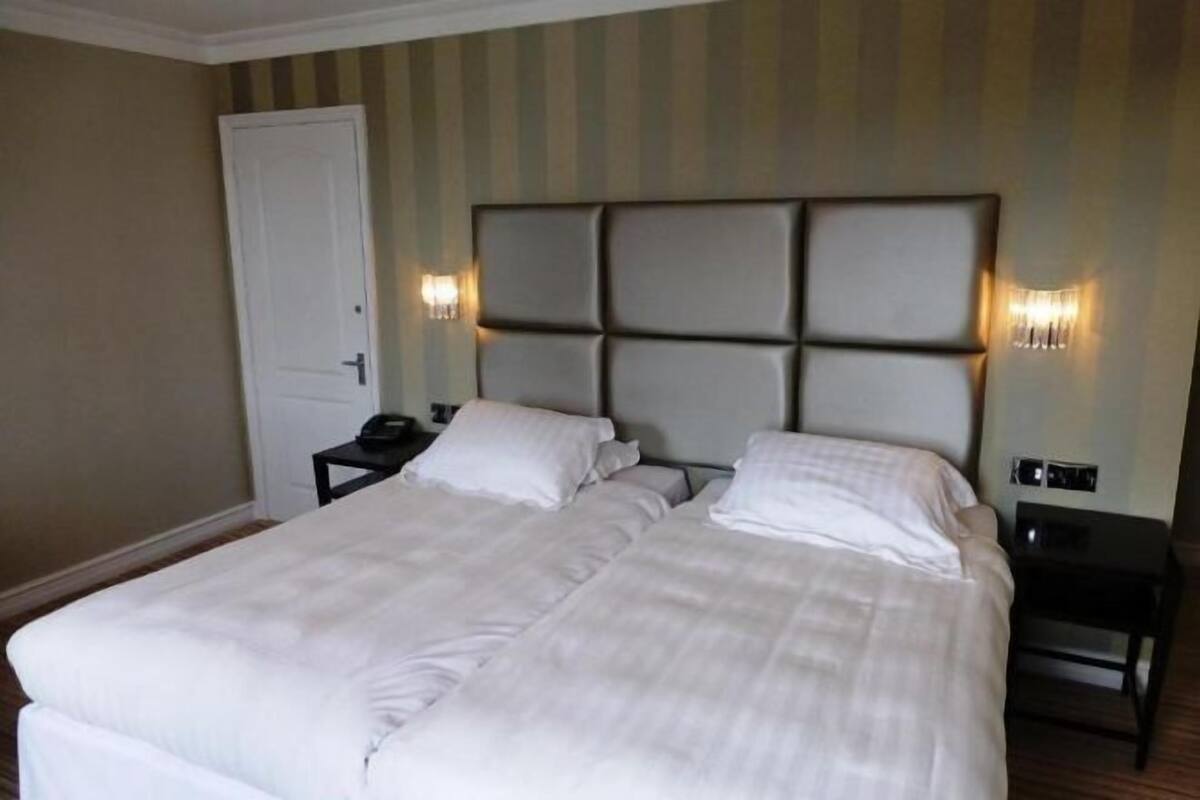 Una cama doble con cabecera acolchada, dos mesitas de noche y una puerta.