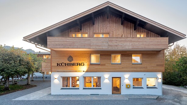 Un edificio de dos pisos con fachada de madera y el nombre "KÜHBERG" en la parte frontal.