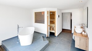 Un baño moderno con una bañera independiente, un tocador de madera con lavabo y una zona de ducha integrada.