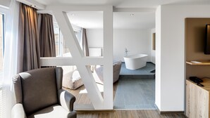 Una habitación de hotel moderna con sofá, bañera y armario de madera.