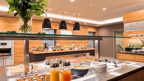 Un bufé con diversas opciones de comida y bebidas, una estación de café y una planta decorativa.