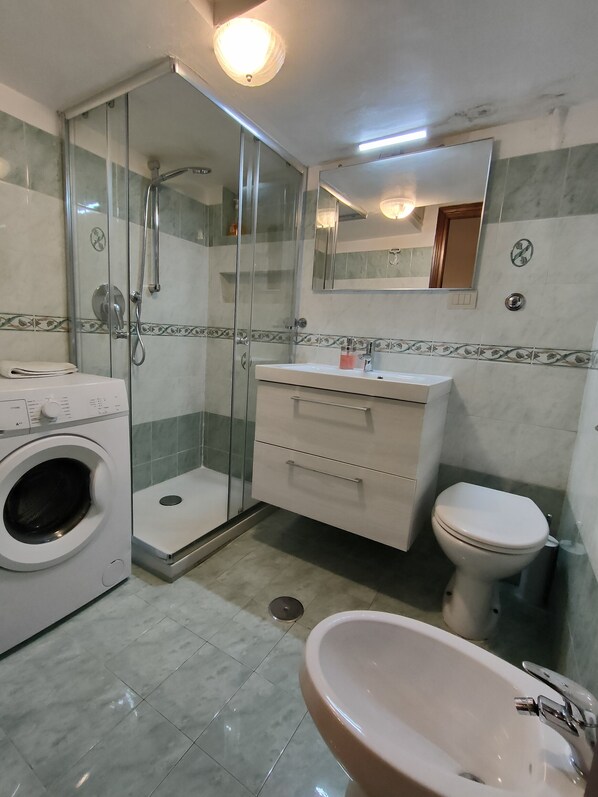 A bathroom with a glass-enclosed shower, a white sink, a toilet, and a washing machine. - Comfortable Apt In Historical Center (2 rooms) (Roma)