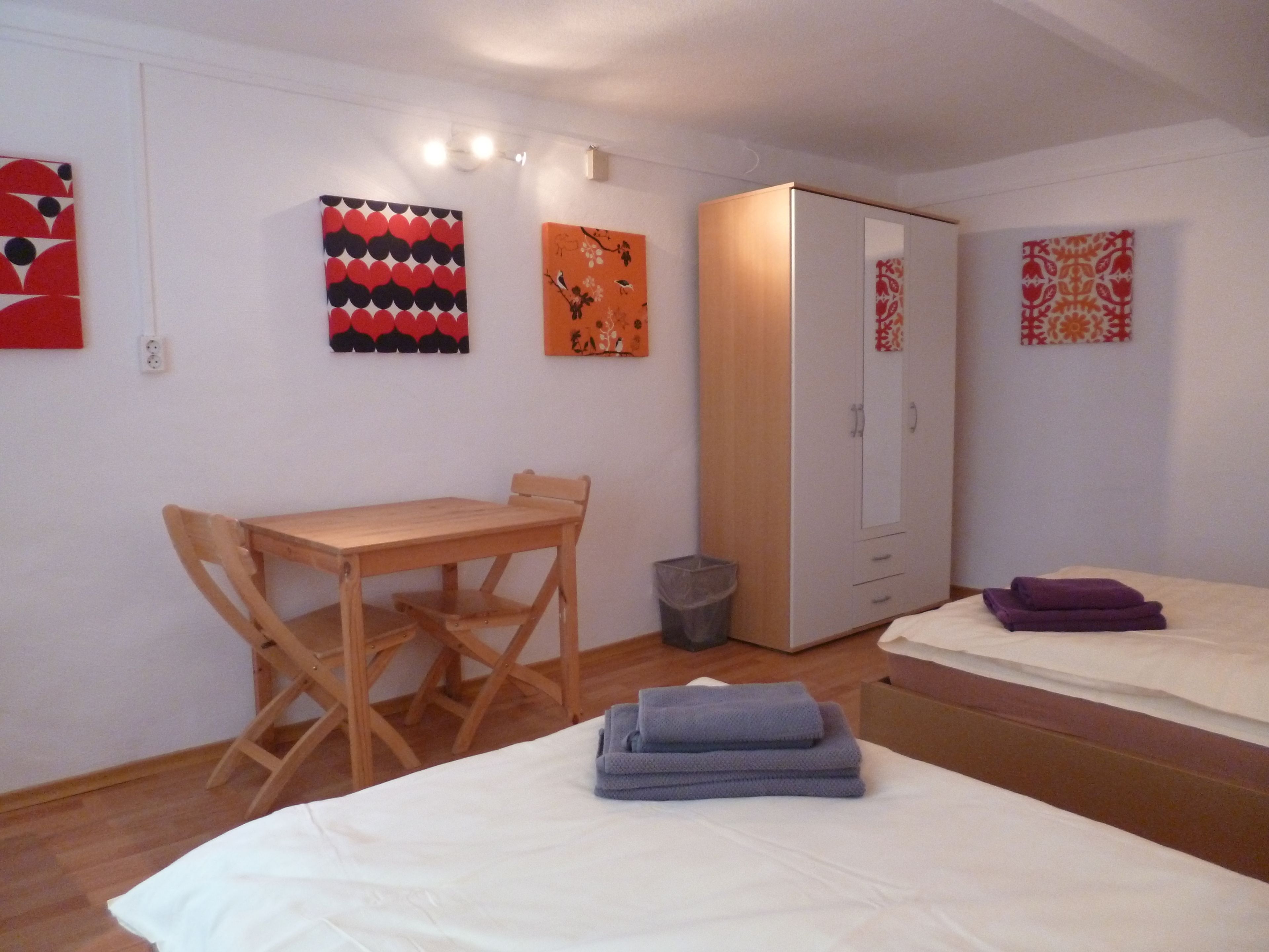 Ein Zimmer mit einem Holztisch, zwei Betten und Bildern an den Wänden.