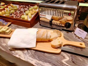 A marble countertop with a cheese slicer, a wooden cutting board with cheese, and a tray of assorted cheeses. - Mercure Wuhan Yangluo (Wuhan)