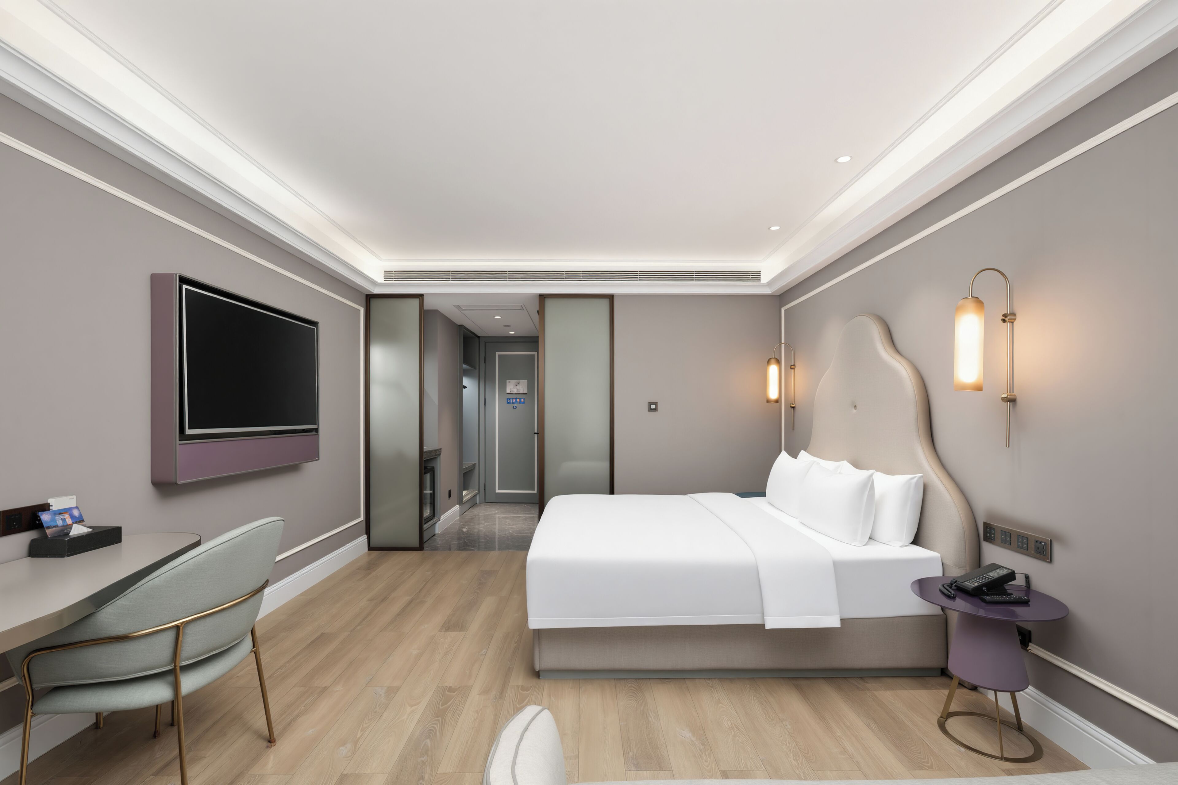 A hotel room with a bed, bedside table, TV, desk, chair, and a bathroom visible through a door.