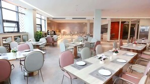 Un comedor moderno con varias mesas y sillas, ventanas amplias y una cocina al fondo.