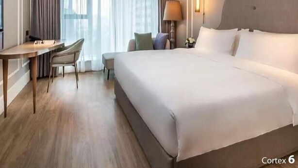 Habitación de hotel con una cama grande, un escritorio, una silla, una lámpara y una ventana con cortinas.