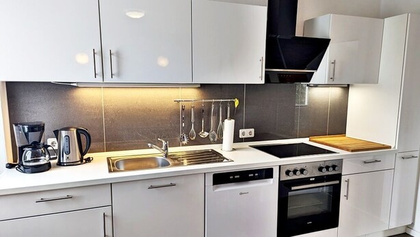 A modern kitchen with white cabinets, a dishwasher, a stove, and a coffee maker. - Gästehaus Koblenz (Koblenz)