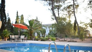 A swimming pool with metal ladders, surrounded by outdoor furniture and trees. - Casa Rural Herrera (Villacarrillo)