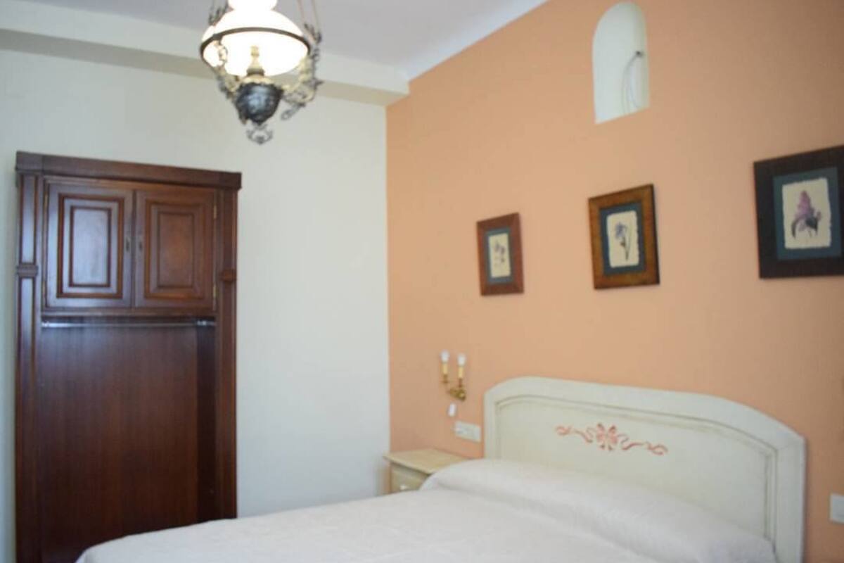A bedroom with a bed, a wooden wardrobe, and framed pictures on the wall.