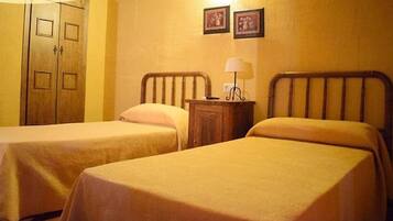 A room with two single beds, wooden headboards, a nightstand with a lamp, and a wardrobe with two doors.