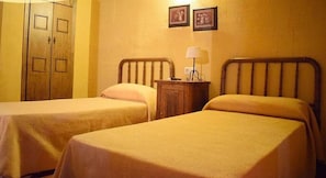 A room with two single beds, wooden headboards, a nightstand with a lamp, and a wardrobe with two doors. - Casa Rural Herrera (Villacarrillo)