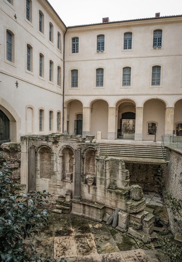 A courtyard with ancient ruins and a building with arched windows and a staircase.