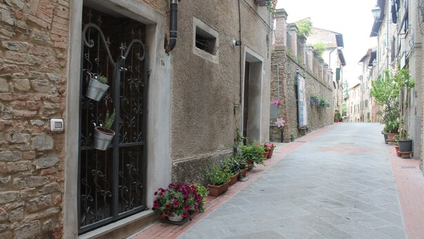 A narrow street with buildings on either side, featuring stone walls and metal gates.